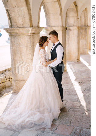Fine-art wedding photo in Montenegro, Perast. Wedding couple cuddles in old stone columns. Fine-art wedding photo in Montenegro, Perast. Wedding couple cuddles in old stone columns. 67008435