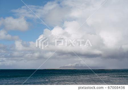 A snow-covered mountain on the Atlantic coast in Iceland. View from the other side, or from the sea. Cloudy weather, dense clouds. A snow-covered mountain on the Atlantic coast in Iceland. View from the other side, or from the sea. Cloudy weather, dense clouds. 67008436