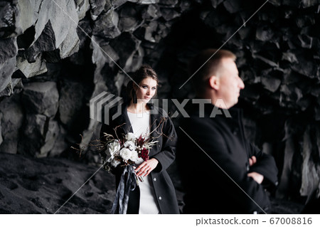 Destination Iceland wedding. Wedding couple under a rock of basalt stones. Bride and groom on the black beach of Vik. 67008816
