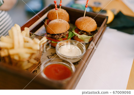Three mini burgers on a tray with two sauces and fries. Three mini burgers on a tray with two sauces and fries. 67009098