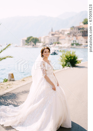 Portrait of a bride in a cream dress under a palm tree on a background of the sea. Fine-art wedding photo in Montenegro, Perast. Portrait of a bride in a cream dress under a palm tree on a background of the sea. Fine-art wedding photo in Montenegro, Perast. 67009328