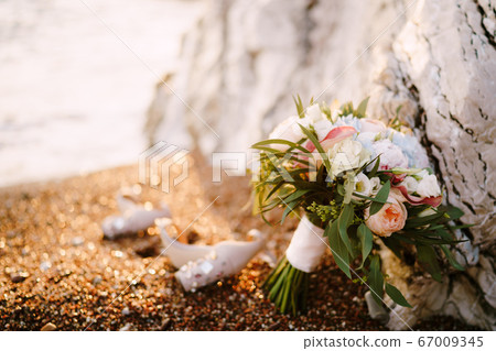 bridal bouquet of white and pink roses, peonies, hortense branches of eucalypt tree, eustoma white ribbons and the shoes of the bride near the rocks on a pebble beach bridal bouquet of white and pink roses, peonies, hortense branches of eucalypt tree, eustoma white ribbons and the shoes of the bride near the rocks on a pebble beach 67009345