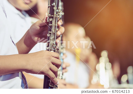 Male student with friends blow the clarinet with the band for performance on stage at night. 67014213