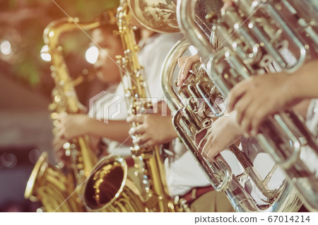 Male student with friends blow the euphonium with the band for performance on stage at night. 67014214