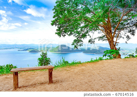 Lookout point with resting wooden bench. Beautiful scenery of nature with a large reservoir above the Srinagarind Dam at Rai Ya Yam view point in Si Sawat District, Kanchanaburi Thailand. Lookout point with resting wooden bench. Beautiful scenery of nature with a large reservoir above the Srinagarind Dam at Rai Ya Yam view point in Si Sawat District, Kanchanaburi Thailand. 67014516