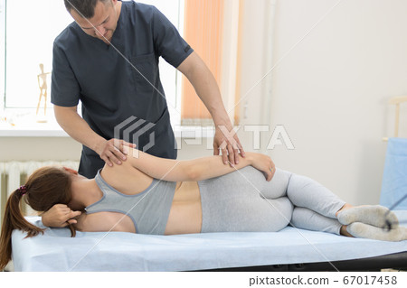 Young woman having osteopathy treatment in the clinic - woman lying on the side and the master making exercises 67017458