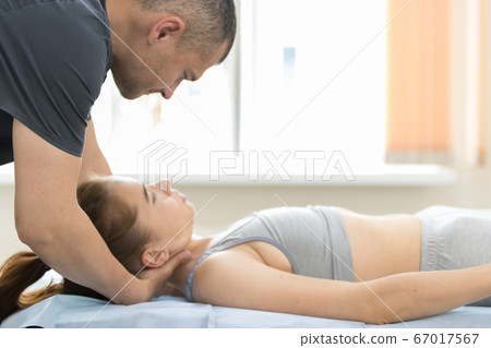 Osteopath treatment in the cabinet - the medical master putting the head of young woman on the pillow Osteopath treatment in the cabinet - the medical master putting the head of young woman on the pillow 67017567