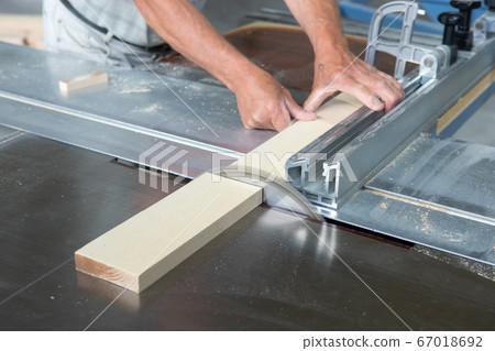 A man cuts a birch board on a circular saw. Circular saw in action. A man cuts a birch board on a circular saw. Circular saw in action. 67018692