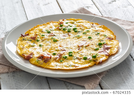 Omelette with prosciutto peas and herbs on white 67024335
