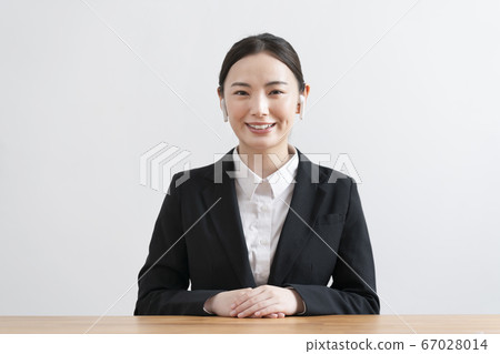 A smiling young woman wearing a suit wearing wireless headphones and talking from the camera's perspective A smiling young woman wearing a suit wearing wireless headphones and talking from the camera's perspective 67028014