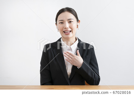 A young woman wearing a suit wearing wireless headphones and looking at the camera 67028016
