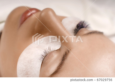 Eyelash Extension Procedure. Close up view of beautiful female eye with long eyelashes, smooth healthy skin. Eyelash Extension Procedure. Close up view of beautiful female eye with long eyelashes, smooth healthy skin. 67029756