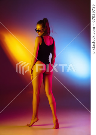 Beautiful seductive girl in fashionable swimsuit on disco bicolored neon studio background in neon light. Summer, resort, fashion and weekend concept 67029759