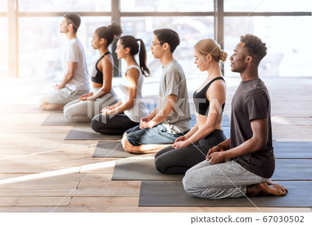 Wellness Concept. Young sporty people in yoga class making meditation exercises together Wellness Concept. Young sporty people in yoga class making meditation exercises together 67030502