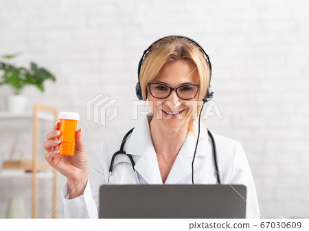 Doctor recommends a medicine. Woman in headphones in white coat holds jar in hand 67030609