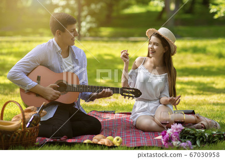Affectionate boyfriend playing guitar and singing song for his girlfriend during summer picnic at park Affectionate boyfriend playing guitar and singing song for his girlfriend during summer picnic at park 67030958