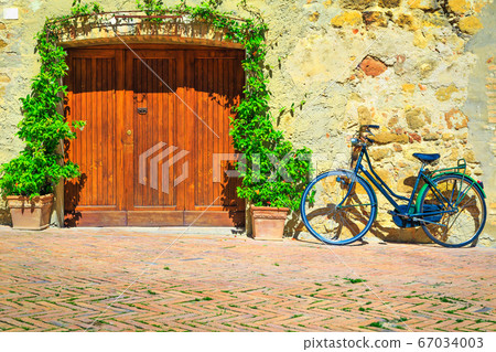 Tuscany street with flowery entrance and retro bicycle, Pienza, Italy 67034003