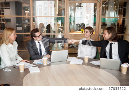 Friendly male colleagues or partners fist bumping at team meetin Friendly male colleagues or partners fist bumping at team meetin 67035522