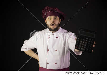 Shocked chef man in uniform holds calculator in panic looks at camera incur loss 67035715