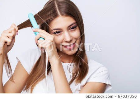 Young woman with luxurious hair straightens it with a curling iron 67037350