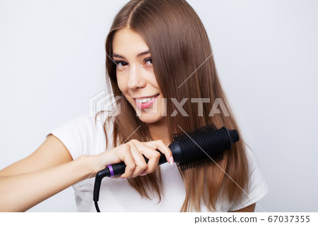 Young woman with luxurious hair straightens it with a curling iron 67037355