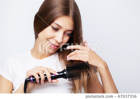 Young woman with luxurious hair straightens it with a curling iron 67037356