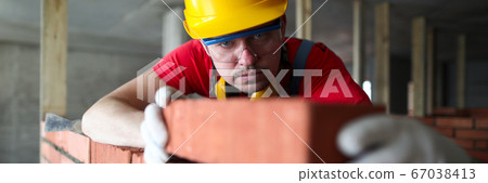 Builder carefully puts red brick on the masonry Builder carefully puts red brick on the masonry 67038413