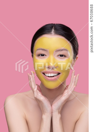 Smiling young woman applying golden face mask 67038688