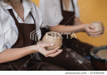 Two women make pottery on a pottery wheels, shaping clay by their hands, close up. Pottery craft workshop at art studio. Two women make pottery on a pottery wheels, shaping clay by their hands, close up. Pottery craft workshop at art studio. 67040484
