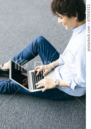 一個男人坐在地板上,使用電腦 一個男人坐在地板上,使用電腦 67050311