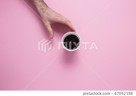 A male hand reaches for a glass with a coffee on a pink background. View from above. A male hand reaches for a glass with a coffee on a pink background. View from above. 67052198