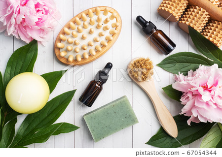 Concept SPA and Wellness. Massage brush, cosmetic oils and soap. Light background with peony flowers. 67054344