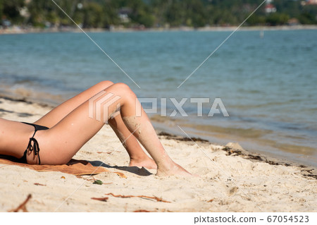 Beautiful slim women's legs on the beach. Lower half of the girl body lying on the beach by the sea. Young women's wet and sun-tanned legs on the beach with the sea view. Beautiful slim women's legs on the beach. Lower half of the girl body lying on the beach by the sea. Young women's wet and sun-tanned legs on the beach with the sea view. 67054523