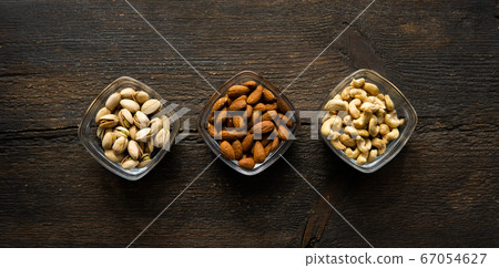 Almond, pistachio and cashew in a small plates which standing on a vintage wooden table. Nuts is a healthy vegetarian protein and nutritious food. Almond, pistachio and cashew in a small plates which standing on a vintage wooden table. Nuts is a healthy vegetarian protein and nutritious food. 67054627