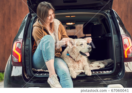 Woman with dog sitting in open trunk of black car 67060041