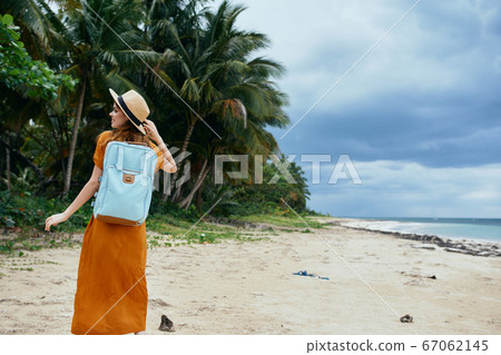A happy traveler with a backpack on her back is walking along the ocean A happy traveler with a backpack on her back is walking along the ocean 67062145