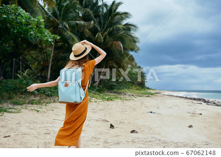 A happy traveler on the island holds a hat on his head and a backpack A happy traveler on the island holds a hat on his head and a backpack 67062148