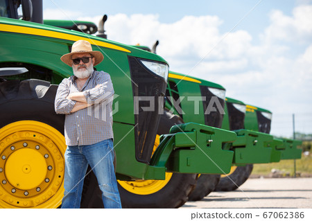 A farmer with a tractor, combine at a field in sunlight. Confident, bright colors A farmer with a tractor, combine at a field in sunlight. Confident, bright colors 67062386