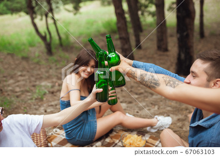 Group of friends clinking beer bottles during picnic in summer forest. Lifestyle, friendship 67063103