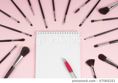Large set of makeup brushes with a notebook and pen mock-up on a pink background. Flat lay 67068281