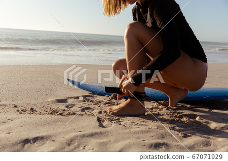 Mid section of woman preparing for surfing on the beach Mid section of woman preparing for surfing on the beach 67071929