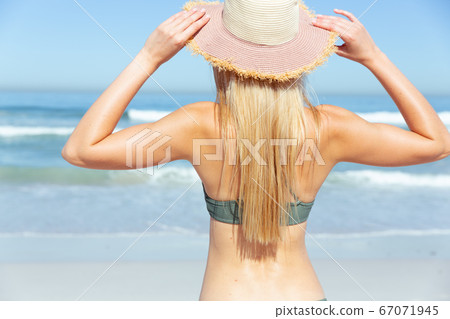 Rear view of woman with hat standing on the beach Rear view of woman with hat standing on the beach 67071945
