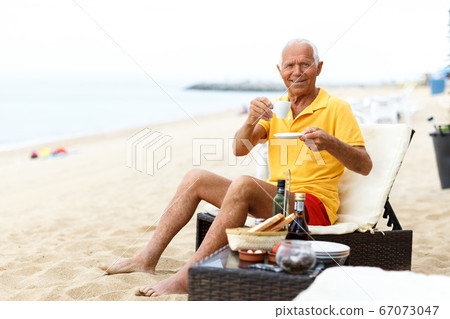 Jolly mature man sitting with cup of hot drink Jolly mature man sitting with cup of hot drink 67073047