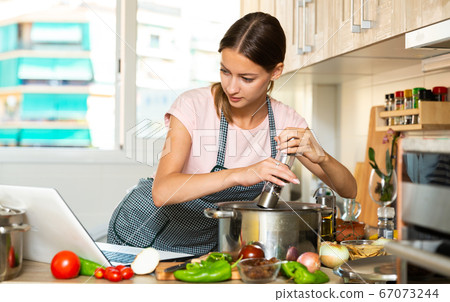 Girl cooking soup with help of laptop 67073244
