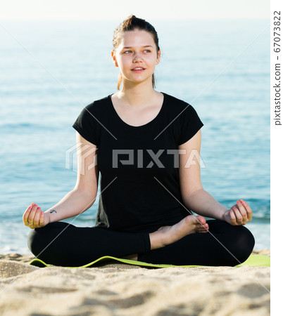 Female 20-30 years old is sitting and doing meditation in black T-shirt Female 20-30 years old is sitting and doing meditation in black T-shirt 67073822