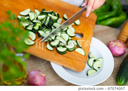 Female hands cut fresh cucumbers for vegetable salad, 67074007