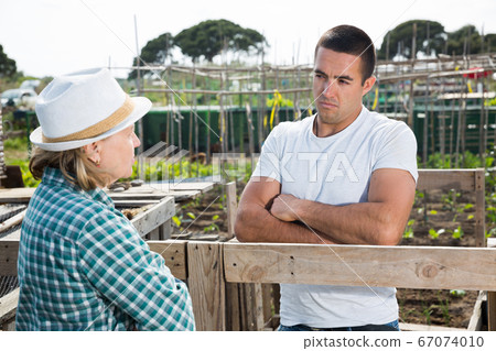 Male horticulturist talking with grandmother near wooden girders Male horticulturist talking with grandmother near wooden girders 67074010