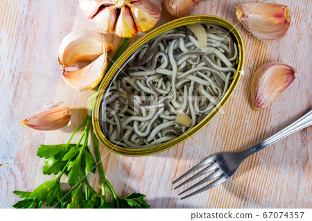 Open tin can of pickled eels and garlic with greens at table Open tin can of pickled eels and garlic with greens at table 67074357