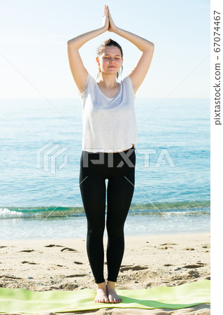 Adult woman in white T-shirt is staying and practicing asana Adult woman in white T-shirt is staying and practicing asana 67074467