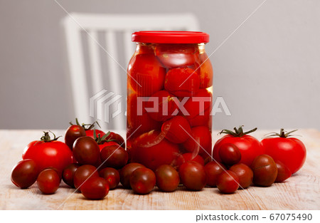 Glass jar with pickled tomatoes and fresh tomatoes 67075490